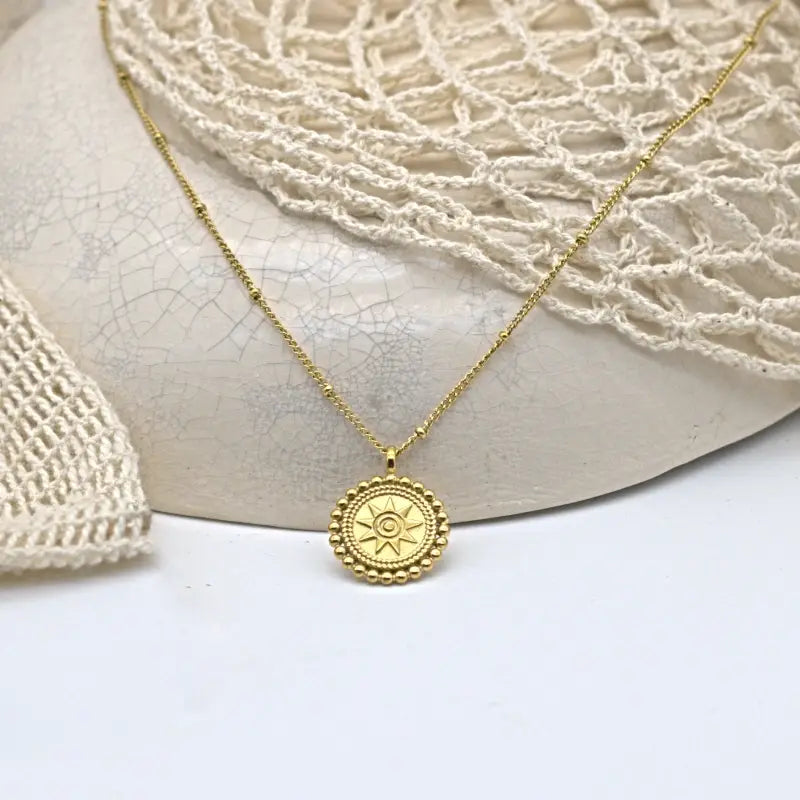 Collier doré chaîne fine avec un pendentif rond gravé de d'un motif étoilé encerclé de petites boules