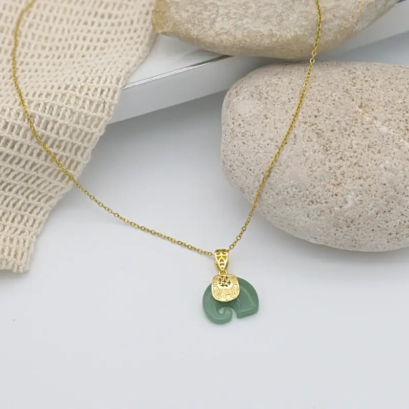 Collier doré chaîne fine avec un  pendentif éléphant en Pierre de Jade et gravure lié par une plaque doré et gravée de motifs ethniques