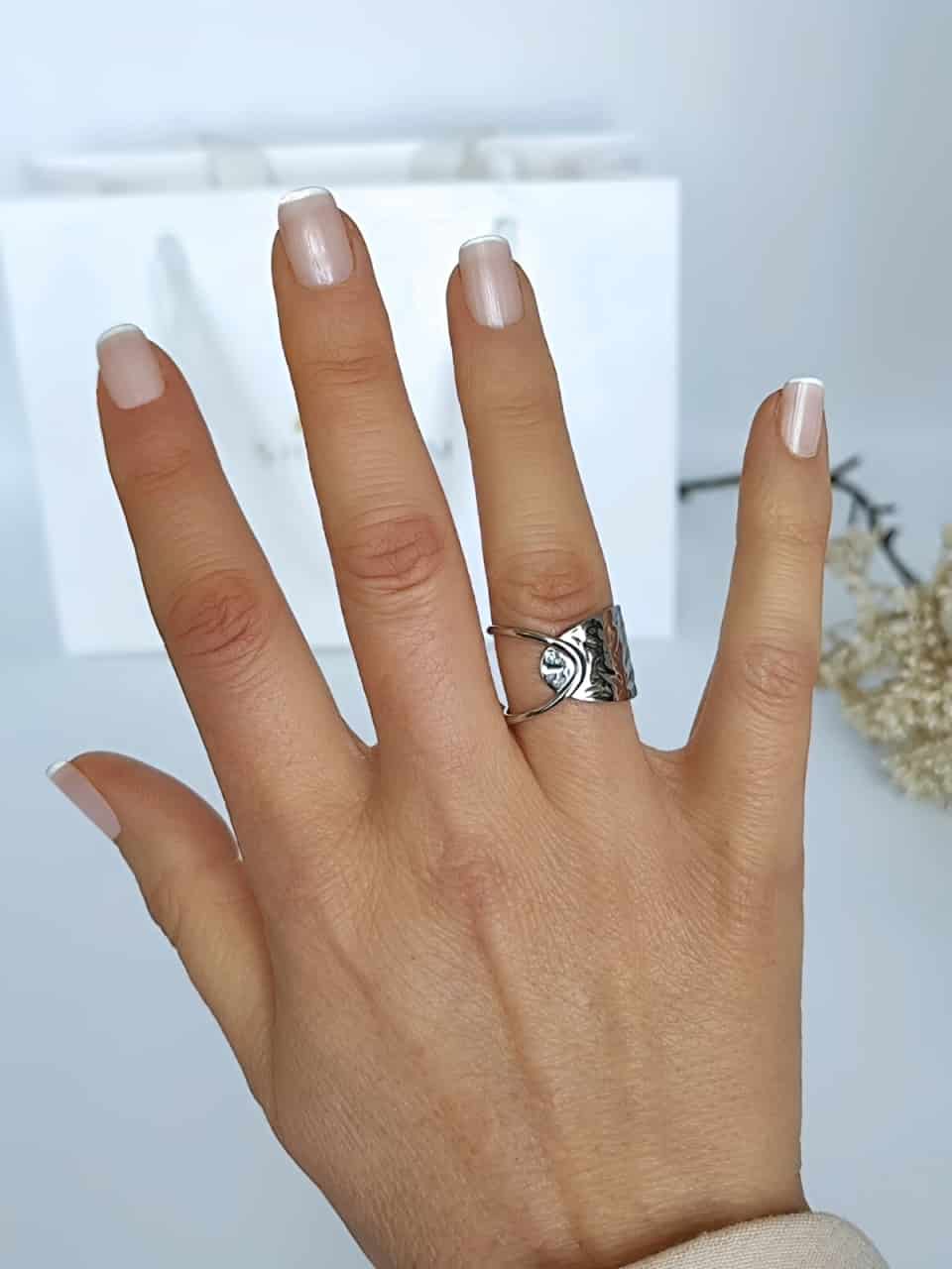 Bague en acier inoxydable argenté, ajourée d'un coté et martelée de l'autre portée au doigt