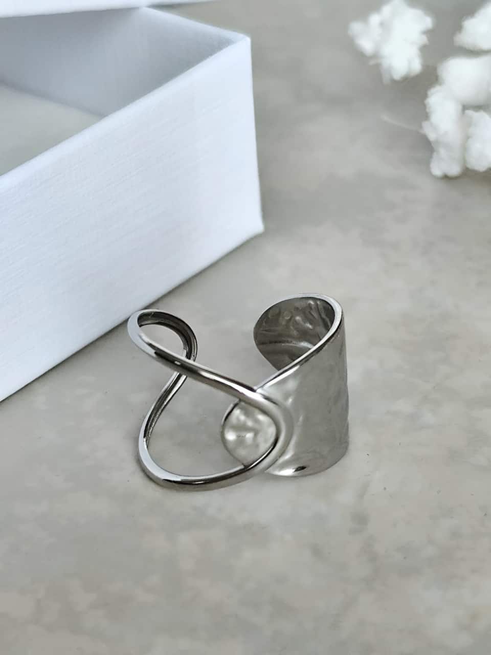 Bague argentée en acier inoxydable ouverte avec une partie large à effet martelé.