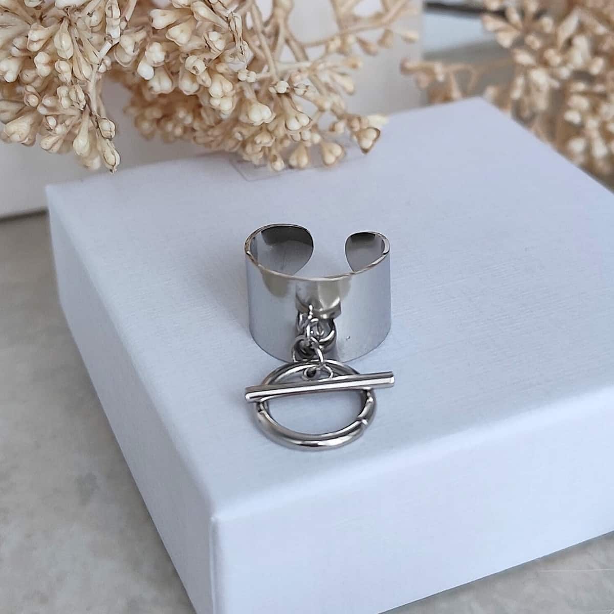 Bague large argentée en acier inoxydable avec breloque circulaire et petite barre.