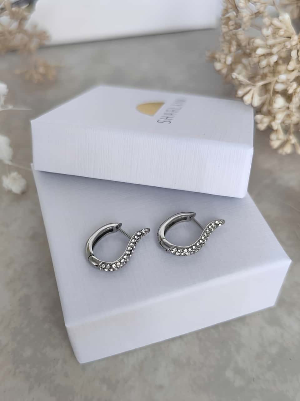 Ces clous d’oreilles en acier inoxydable de forme arrondie sertis de zircons posés sur un joli écrin blanc