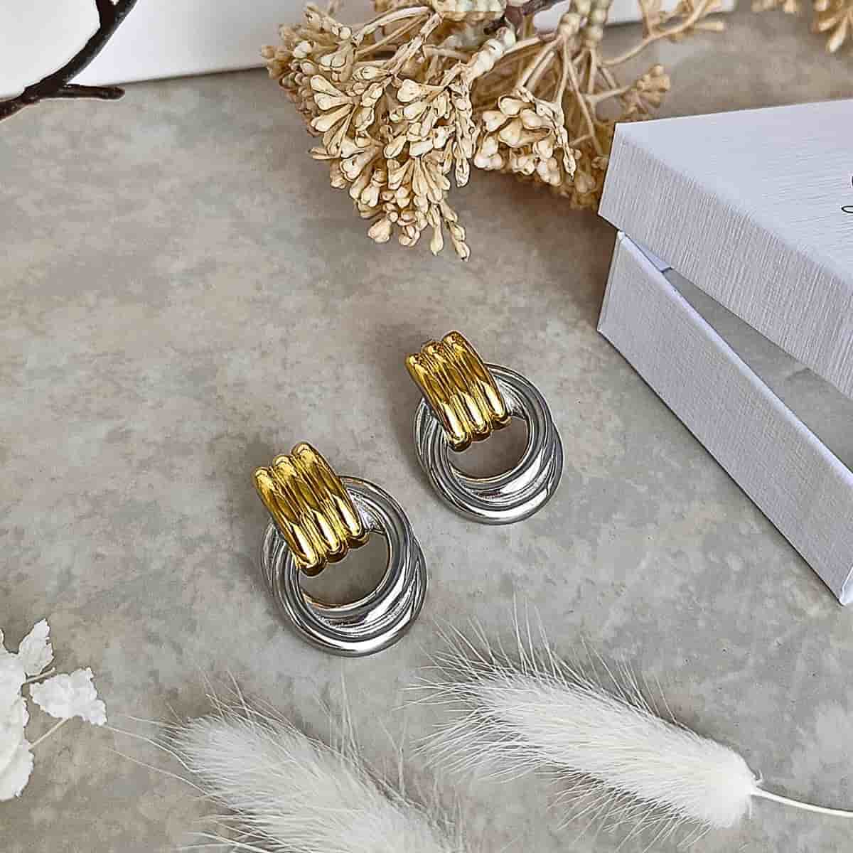Boucles d’oreilles acier inoxydable bicolores, partie supérieure dorée striée et anneaux argentés entrelacés.