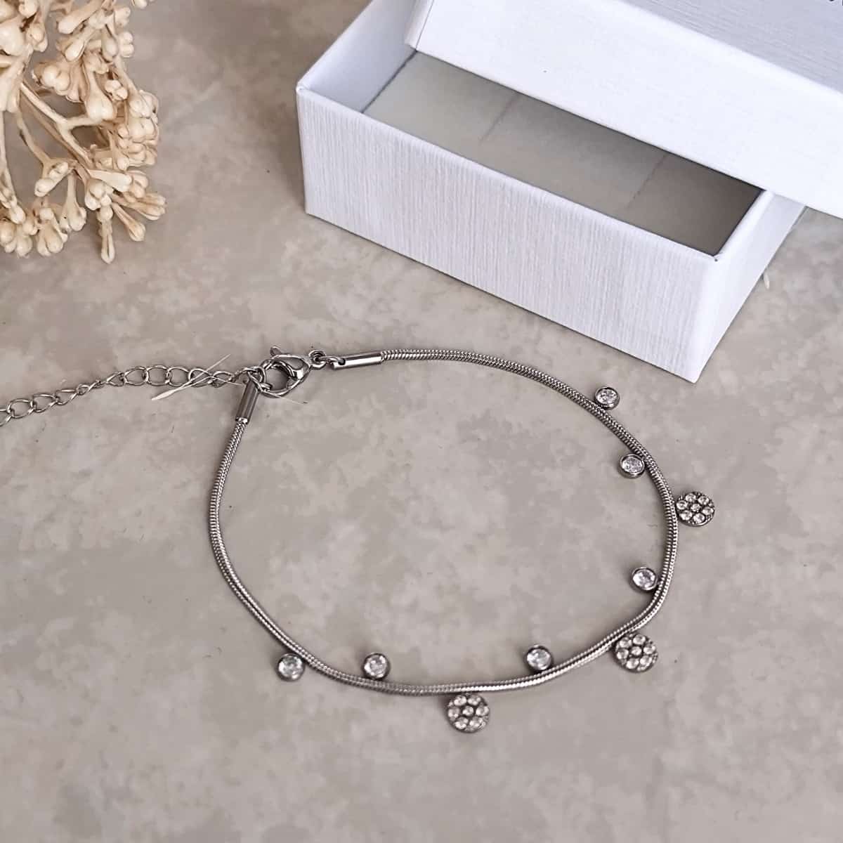 Bracelet en acier inoxydable fin, argenté avec de petits pendentifs alternés  porté sur le poignet