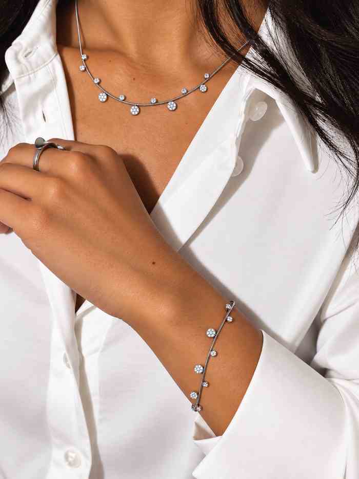 Bracelet en acier inoxydable fin, argenté avec de petits pendentifs en zircons et forme de fleur porté par un modèle