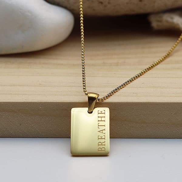 Collier doré avec un pendentif rectangulaire représentant une plaque gravée Breathe