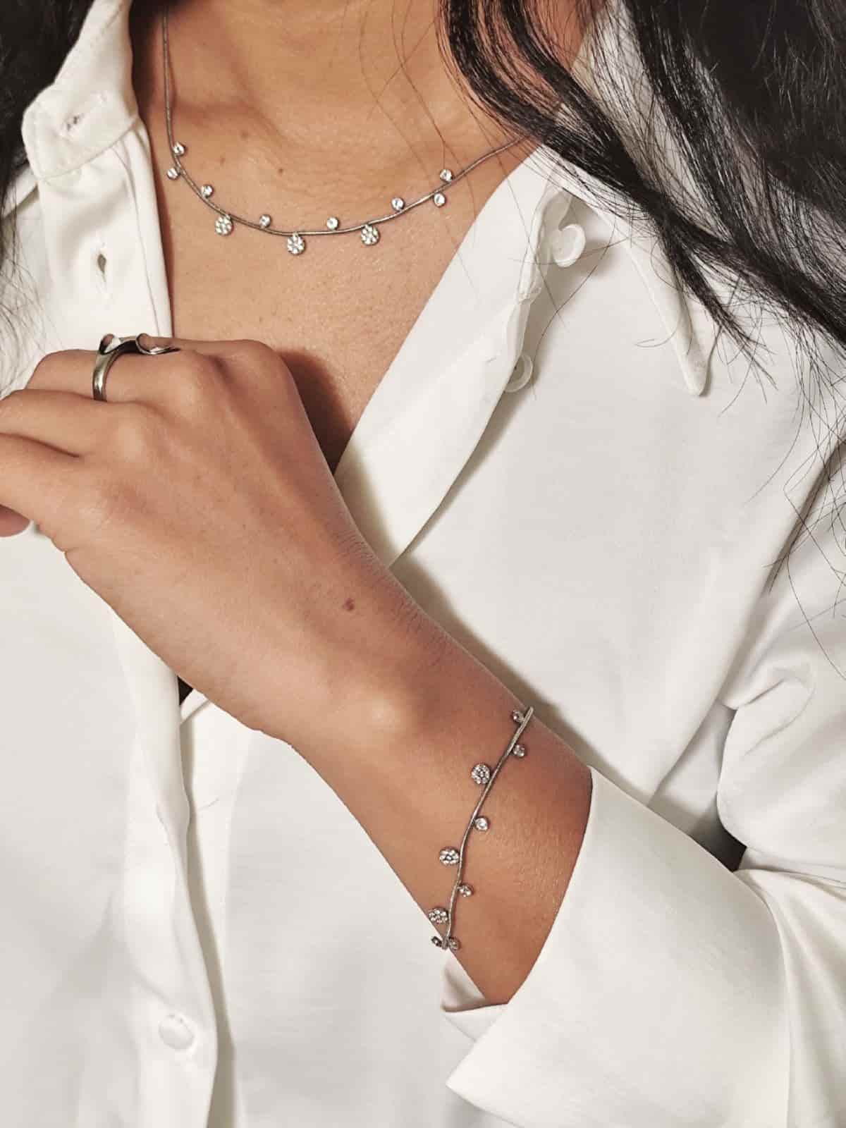Collier ras de cou en acier inoxydable fin, argenté avec de petits pendentifs alternés  porté sur un modèle