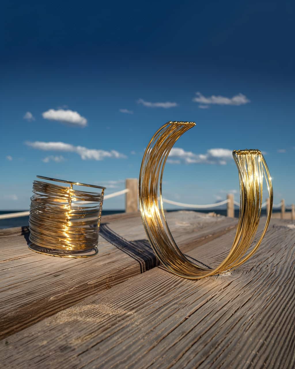 ensemble collier et manchette dorée en acier inoxydable large en forme de spirales posés sur une table en bois en bord de mer