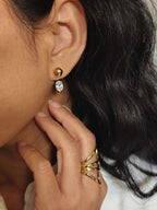 Boucles avec une boule au niveau du lobe et un anneau fin qui revient de derrière jusqu’à l’avant, serti d’un diamant portées à l'oreille